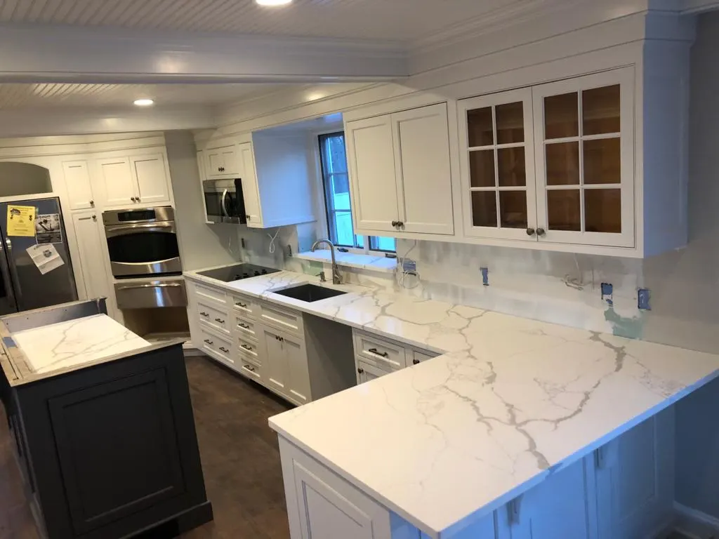 White L-shaped kitchen with veined countertops and a stone backsplash
